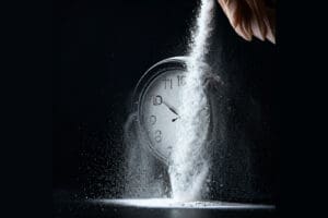 A hand pours a stream of white powder over a clock, with scattered powder on the surface.